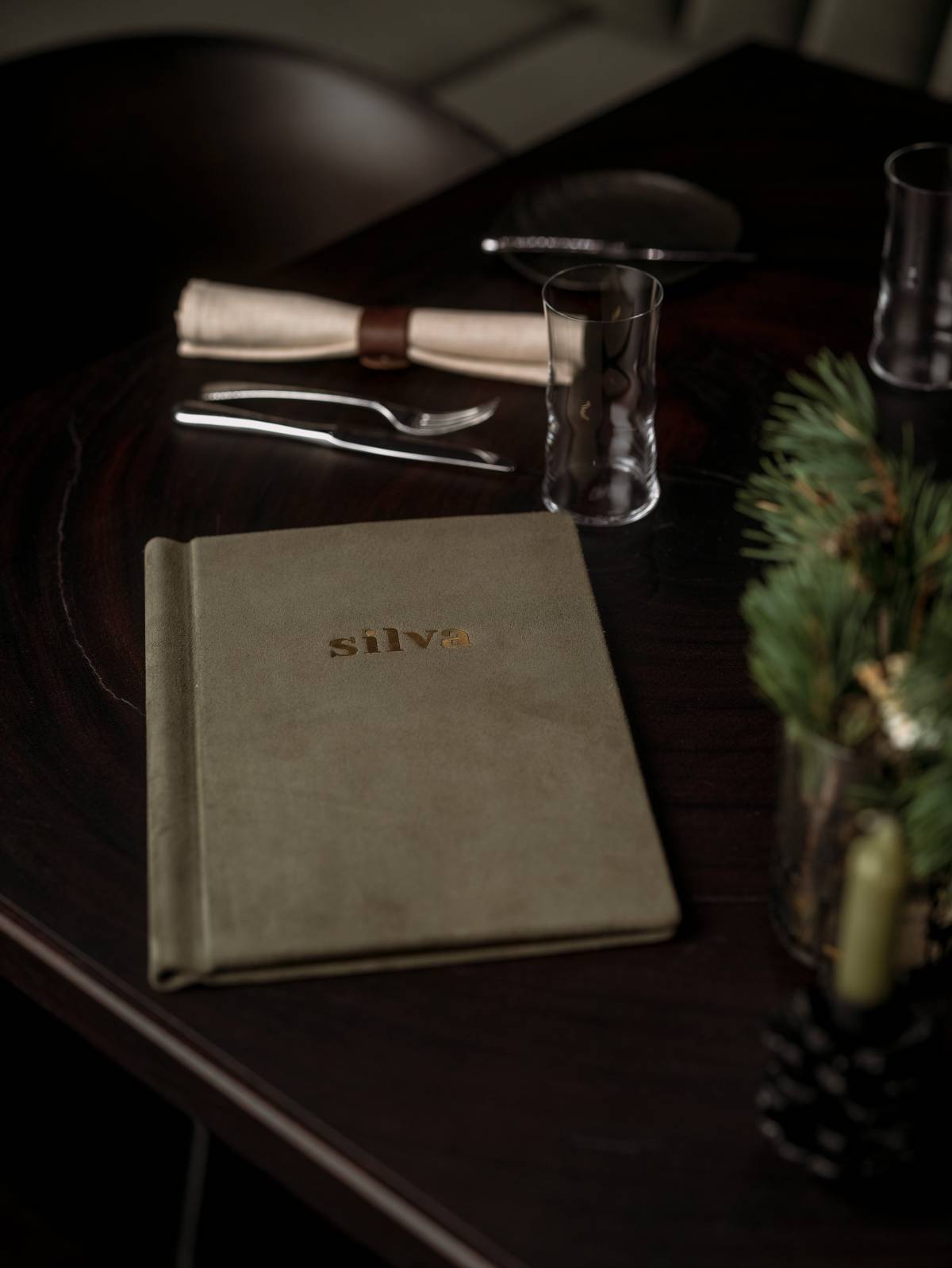 Stilvoll gedeckter Tisch im Restaurant silva mit Speisekarte, Stoffserviette und Tannendeko.